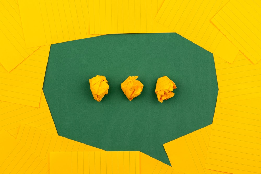 orange sheets of paper lie on a green school board and form a chat bubble with three crumpled papers.