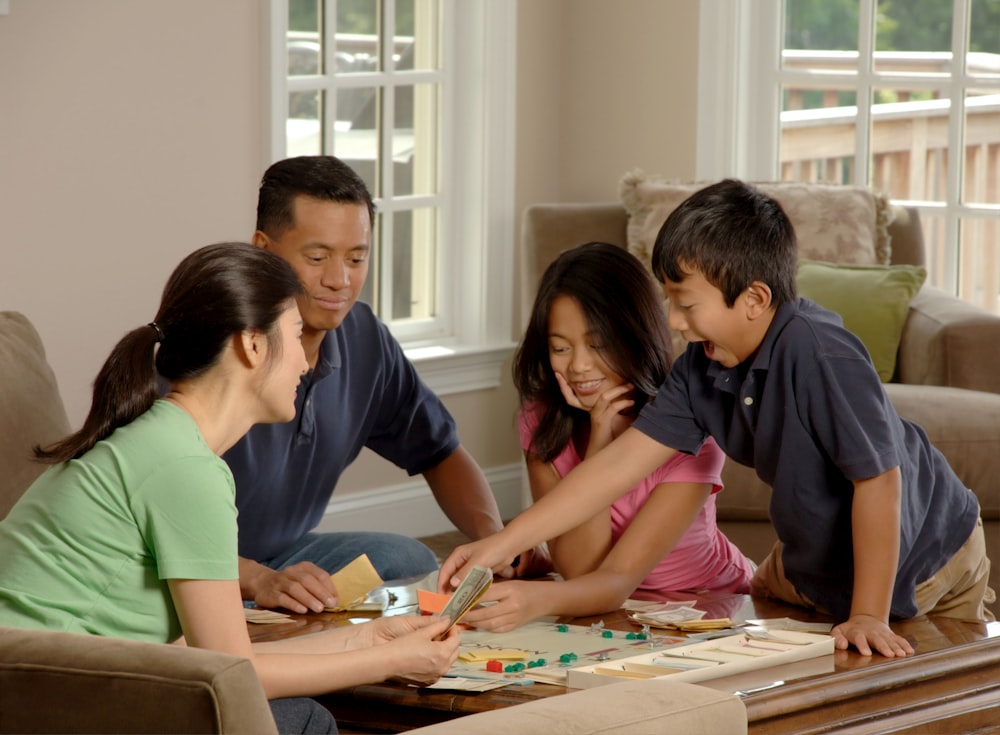 Family Playing A Board Game. An Asian family (adult male and female and two adolescents, male and female) sitting around a coffee table playing a board game. Photographer Bill Branson