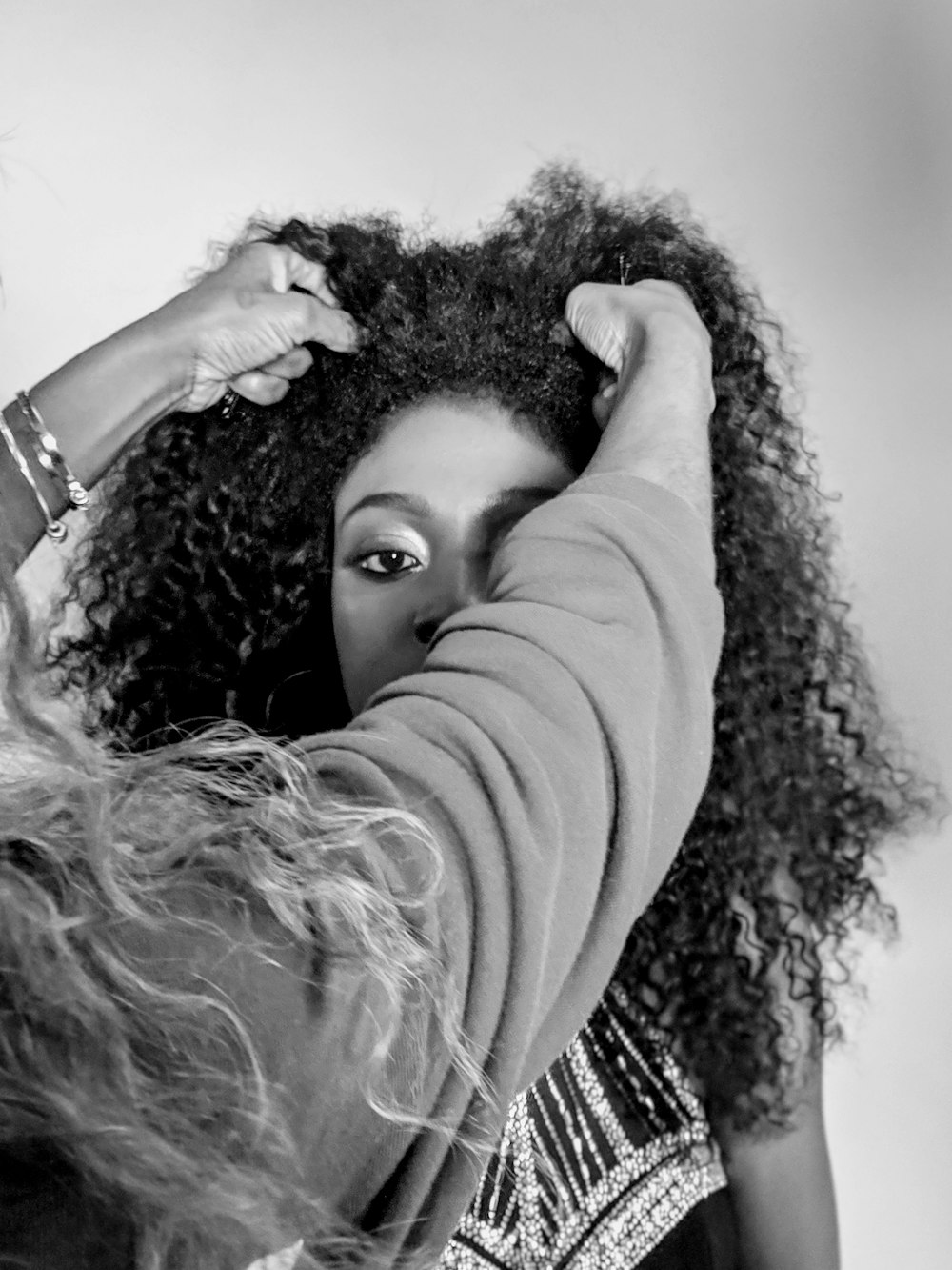 A model wearing a black gown stares into the camera as her stylist works on her hair. 