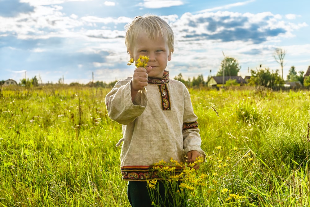 a small blond boy in a traditional Russian shirt in a meadow covered with yellow flowers