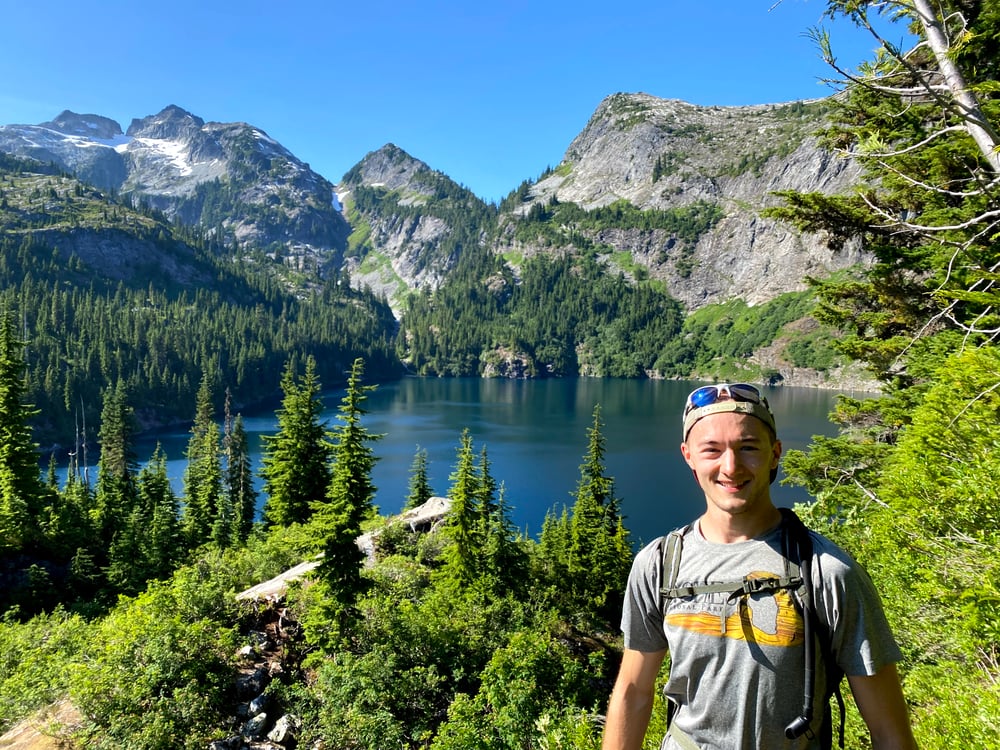 Paul stands in front of Thorton Lake - surrounded by pine trees and rocky mountain peaks - at North Cascades National Park