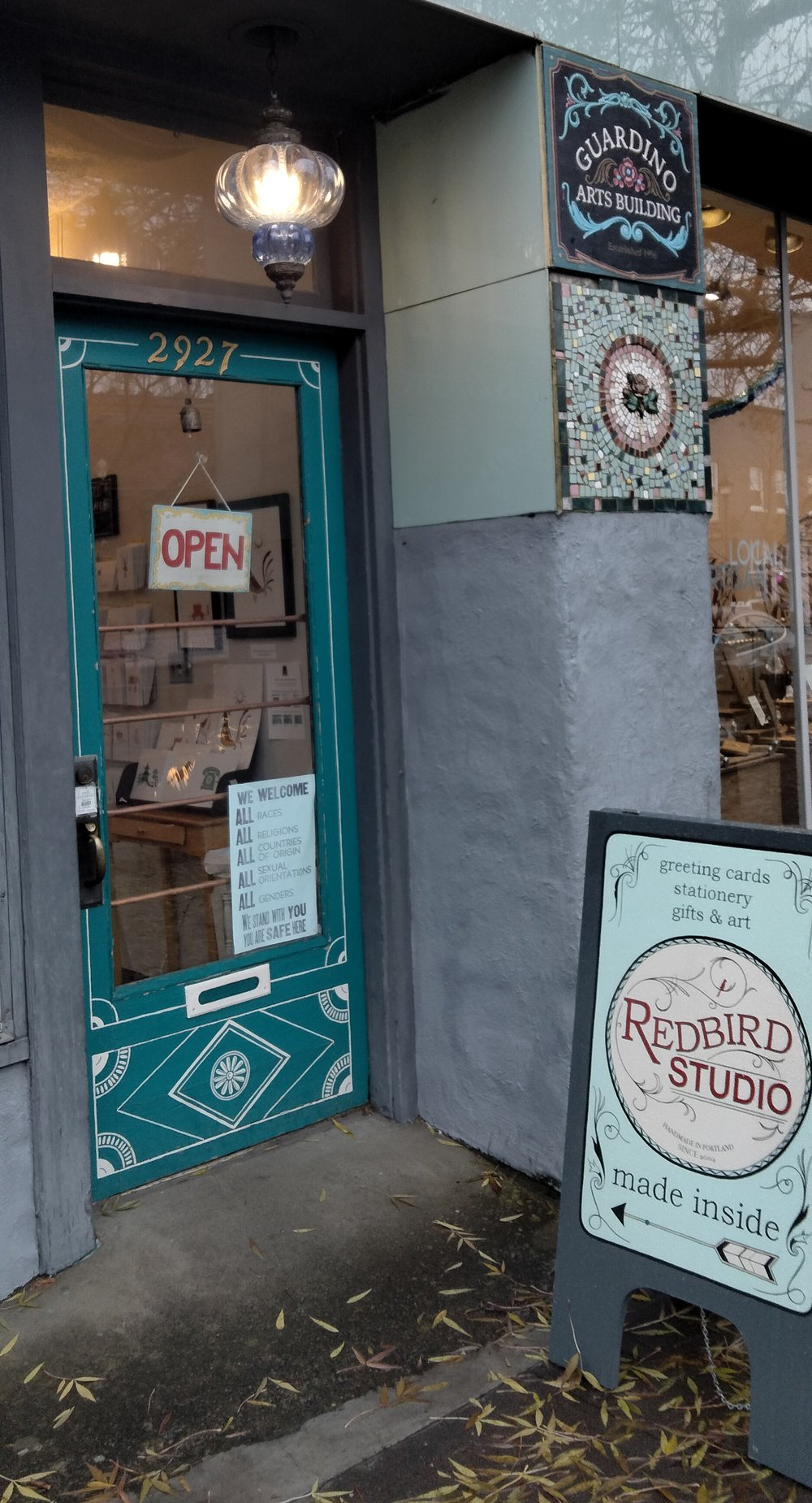Photo of the front door of the studio- blue green with white designs surround the window.  An A-frame sign points to the door and reads 