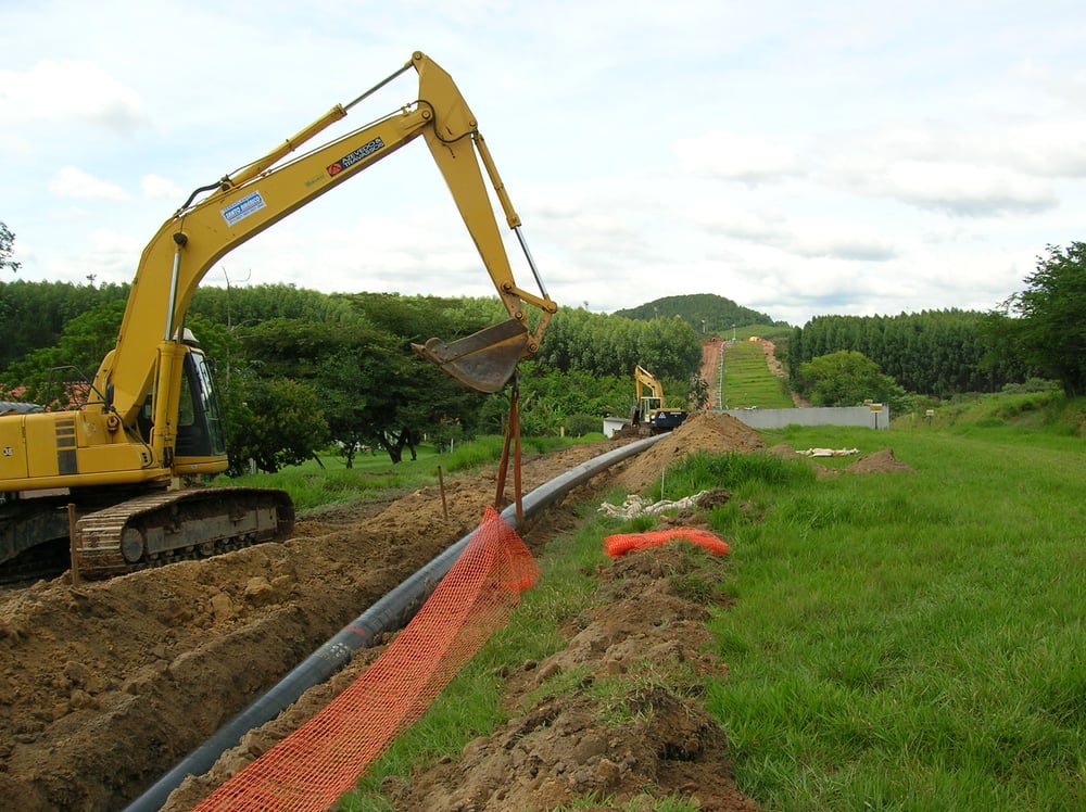 Obras de instalação do Gasoduto RECAP. Uma escavadeira posiciona o tubo do gasoduto dentro de uma vala.