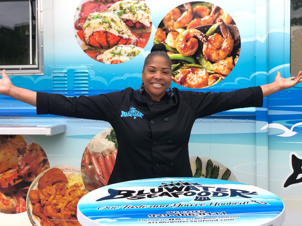 Woman standing, with arms stretched behind table  and in front of seafood truck
